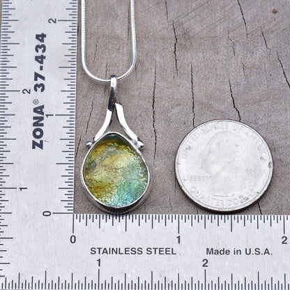 Gold and aqua teardrop dichroic glass pendant beside a ruler and quarter, about 1½ inches long including the bail