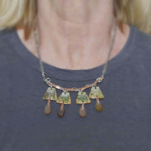 Statement necklace in mixed metals of sterling silver and copper with green tortoise motif enameled copper dangles holding amber sea glass with sterling silver rivets.