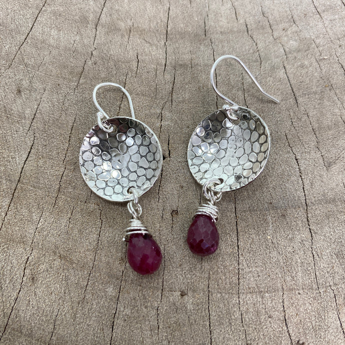 Earrings crafted from disks of hammer textured sterling silver accented with dangles of ruby briolettes (E798)